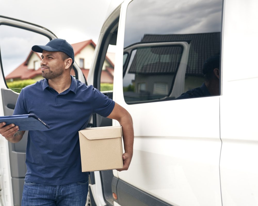 man-courier-with-parcel-looks-around-by-a-delivery-car.jpg